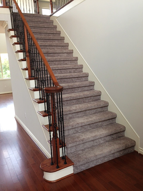 Carpeted staircase with over-the-top handrail and rod iron basket spindles