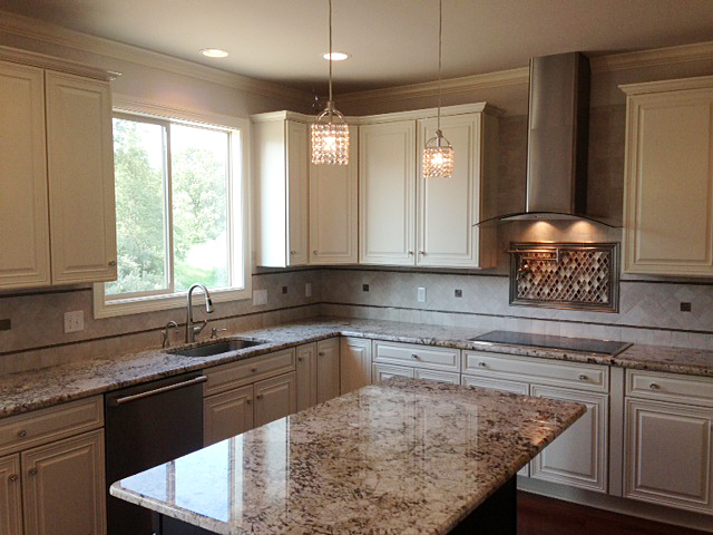 Kitchen featuring white painted cabinets, granite counter tops, stainless hood vent and pot filler